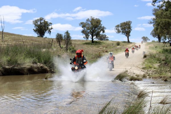 Variety Postie Bike Dashers riding through water on the 2022 Postie Bike Dash event.