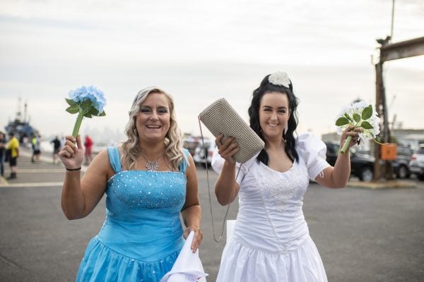 Two women smiling in costume. One is wearing a wedding dress and the other is dressed as a bridesmaid.
