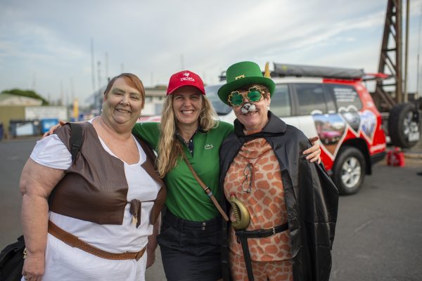 Three people smiling at the camera. The two on the outside are both in bright costumes.