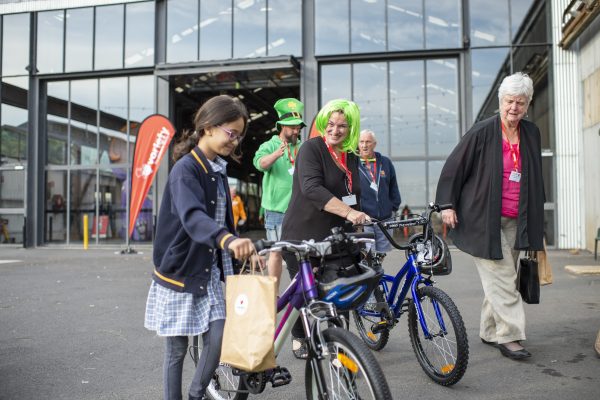 Child and woman holding bikes. The woman is wearing a green wig.